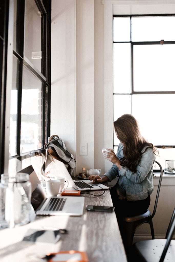 Woman with long brown hair works on a laptop that is sitting on a cluttered countertop